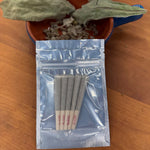 Two whole dried mullein leaves and crumbled leaf in a blue enamel dish above an open mylar bag holding five prerolls